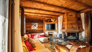 Ein gemütliches Blockhaus-Interieur mit Wohnzimmer, Sofa, Ledersesseln, Kamin und Fernseher.