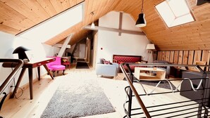 A spacious loft with a high ceiling, wooden beams, a staircase, a red sofa, a grey armchair, and a wooden coffee table. - Gite de Groupe Lozère Aubrac (Peyre en Aubrac)