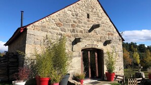A stone church with a red roof, a wooden door, and potted plants in front. - Gite de Groupe Lozère Aubrac (Peyre en Aubrac)