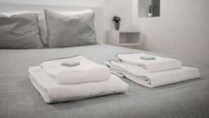 Una cama bien hecha con toallas blancas dobladas y un objeto rectangular pequeño a cada lado.