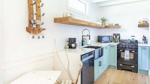 Eine moderne Küche mit Einbauherd, Kaffeemaschine und Mikrowelle. Darüber befinden sich Holzregale, und eine Wandhalterung zeigt Tassen.