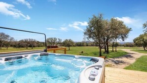 Een hottub met een houten terras, omringd door bomen en een heldere lucht.