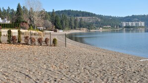 Ein Strand mit einer Umzäunung, Bäumen und Gebäuden im Hintergrund.