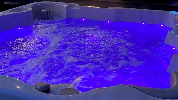 Ein Whirlpool mit blauer Beleuchtung, ein Fernseher und Sitzgelegenheiten im Freien.