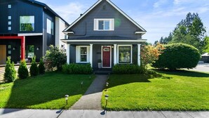 Une maison à deux étages avec un porche à l’avant, une porte rouge et une pelouse bien entretenue.