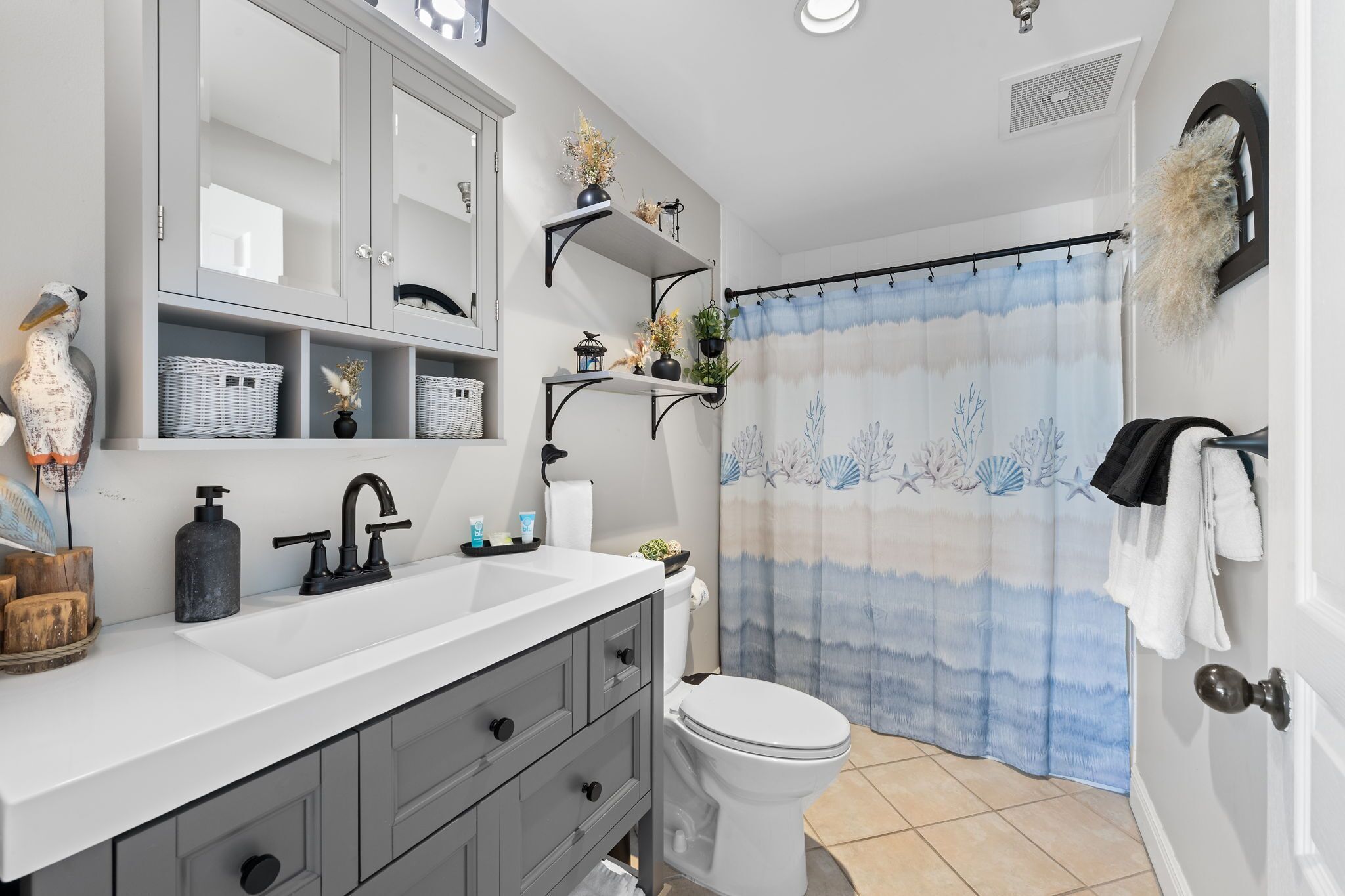 A bathroom with a white sink, dark-toned cabinets, a toilet, and a shower curtain with a sea-themed design.