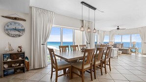 A dining area with a view of the ocean, a round wooden table, and a shelf with decorative items. - Breathtaking Gulf Views! Community Pool! Steps to the Gulf! (Pensacola Beach)