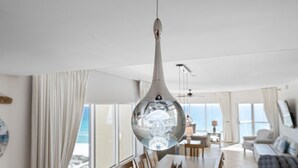A modern dining area with a large table, chairs, and a unique spherical chandelier. - Breathtaking Gulf Views! Community Pool! Steps to the Gulf! (Pensacola Beach)