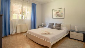 A bedroom with a bed, two bedside tables, a radiator, and a window with blue curtains. - 5-bed chalet in Albir, with swimming pool, AC, 20-min-walk to beach.  (l'Alfàs del Pi)