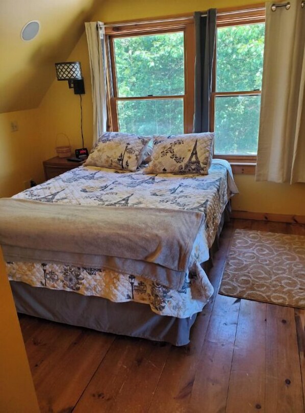 Un dormitorio con una cama, una mesita de noche, una lámpara y una ventana con cortinas.