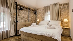 A bedroom with a stone wall, wooden bed frame, two bedside tables with lamps, and a hanging rack. - Lovely home in Zmijavci with private swimming pool, can be inside or outside (Zmijavci)