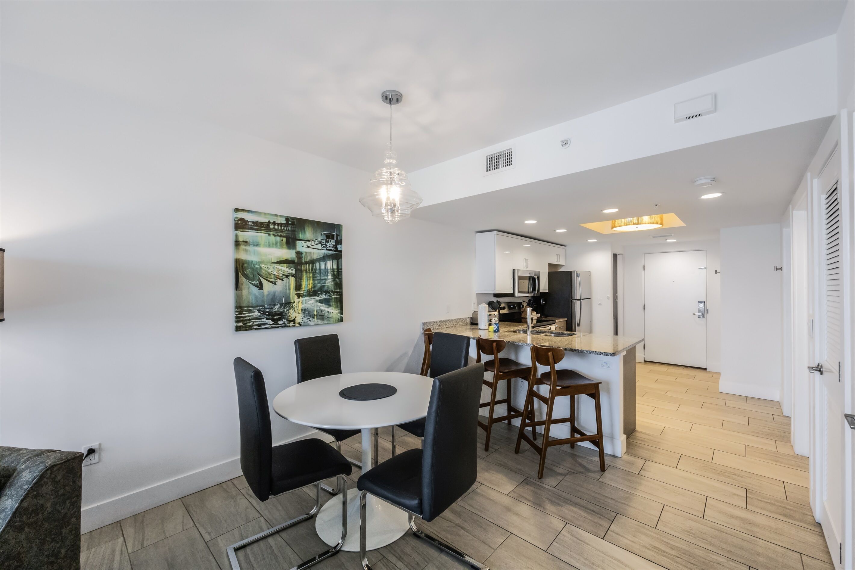 Un espace repas moderne avec une table ronde et des chaises, une cuisine en arrière-plan et un tableau accroché au mur.