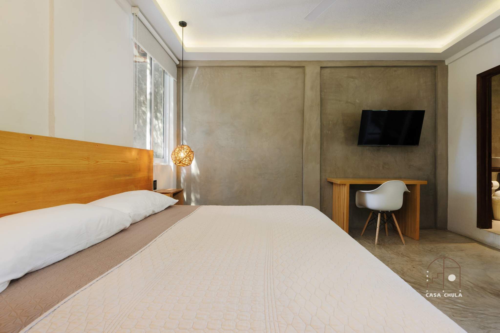 A bedroom with a large bed, a desk, a chair, a television, and a window.