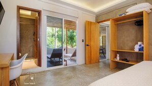 A modern hotel room with a large bed, a wooden wardrobe, a seating area with a table and chairs, and a sliding glass door leading to an outdoor patio. - Incredible Nautilus Suite in the Heart of Punta (Brisas de Zicatela)