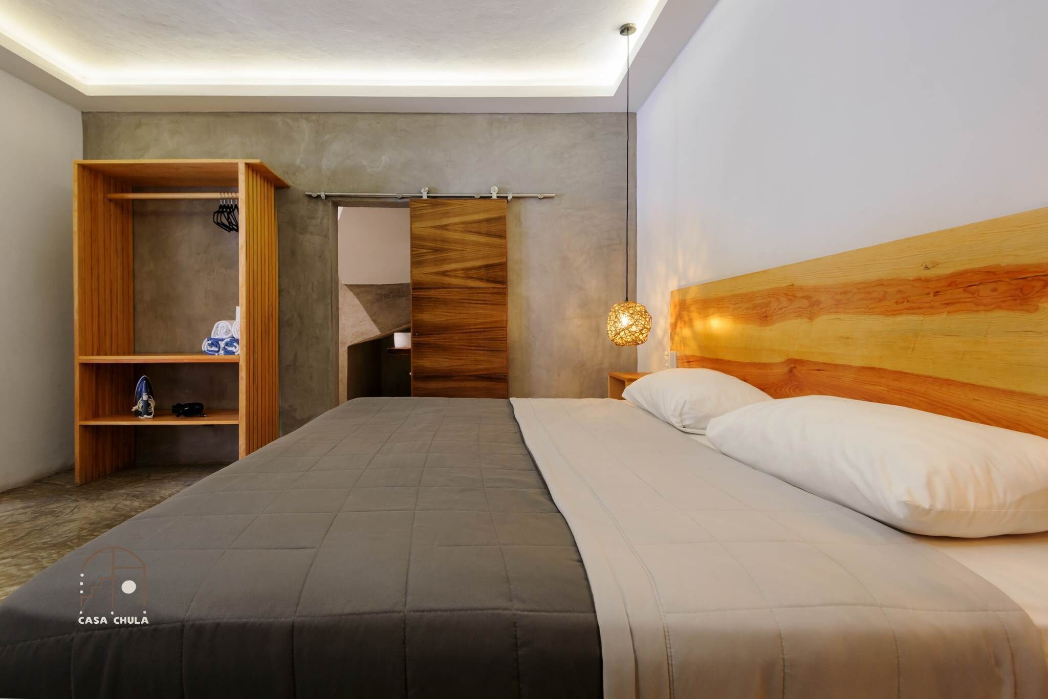 A modern hotel room with a large bed, wooden wardrobe, and a unique headboard.