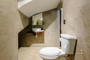 Une salle de bain avec des toilettes blanches, une étagère en bois au-dessus du lavabo et un miroir au mur.