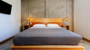 A modern bedroom with a wooden headboard, a large bed with grey bedding, two bedside tables with lamps, and a flat-screen TV mounted on the wall. - Unmatched Modern PH Loft in the Center of la Punta (Brisas de Zicatela)