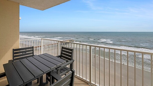A balcony with a table and chairs overlooking the ocean.