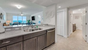 A modern kitchen with a large island, a built-in dishwasher, and a view of the ocean through large windows.