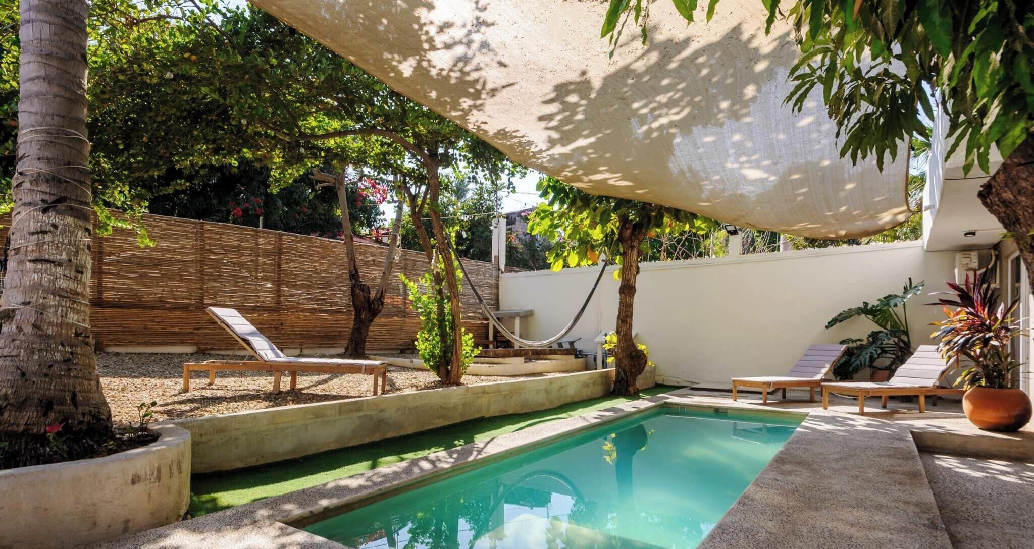 Un jardin avec une piscine, des chaises longues et un hamac.