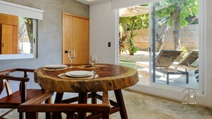 A dining area with a round wooden table, chairs, and a view of a pool and garden through large sliding glass doors. - Spectacular Suite Steps Away From Center La Punta! (Brisas de Zicatela)