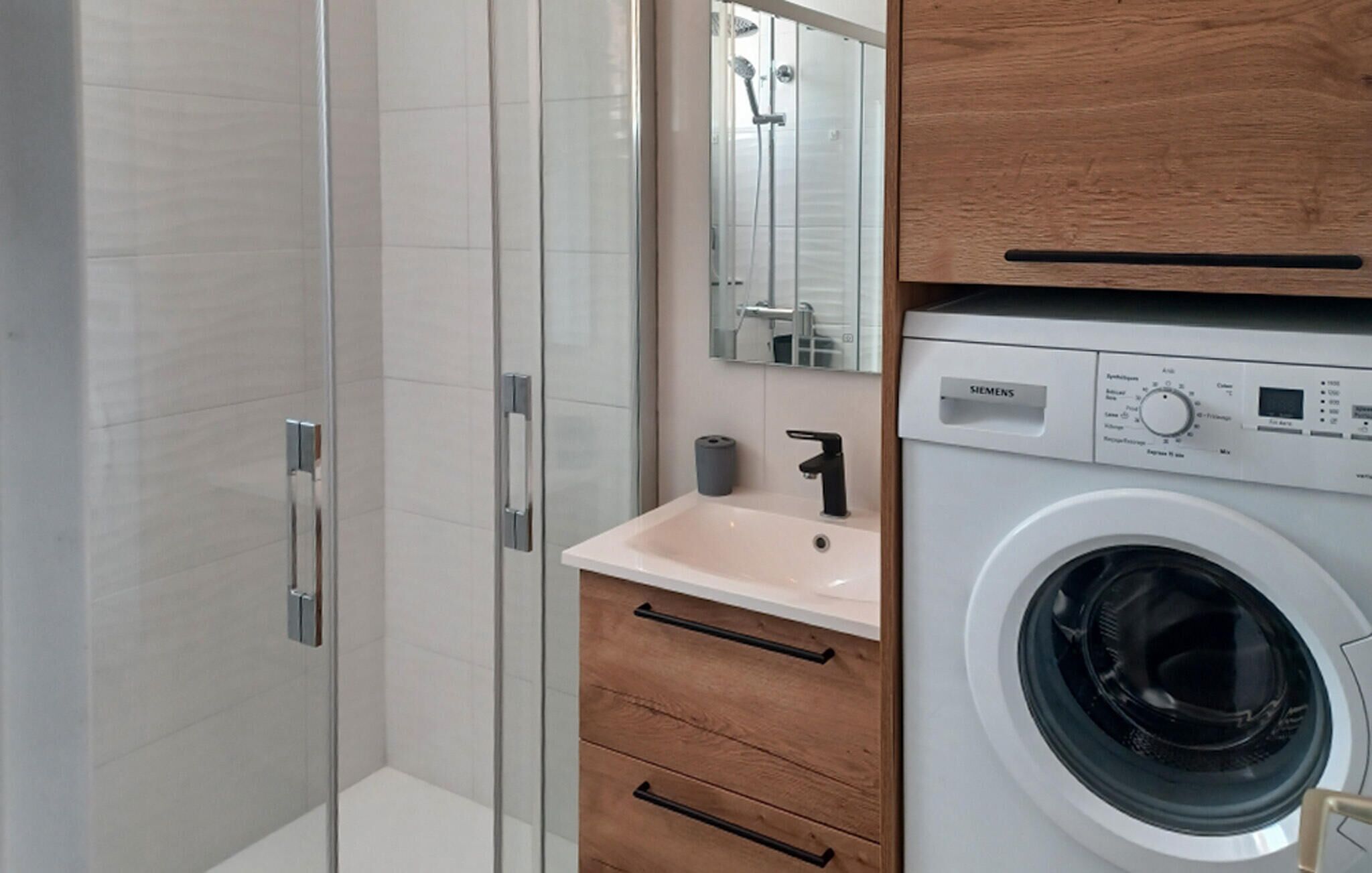 A modern bathroom with a glass shower enclosure, a sink with a mirror, and a front-loading washing machine.