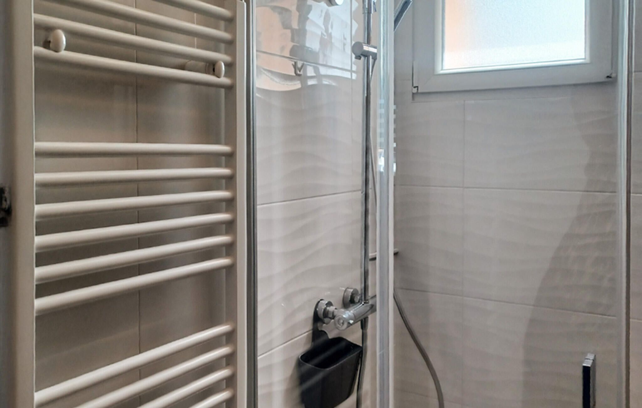 A bathroom with a towel rack, a shower, and a window.