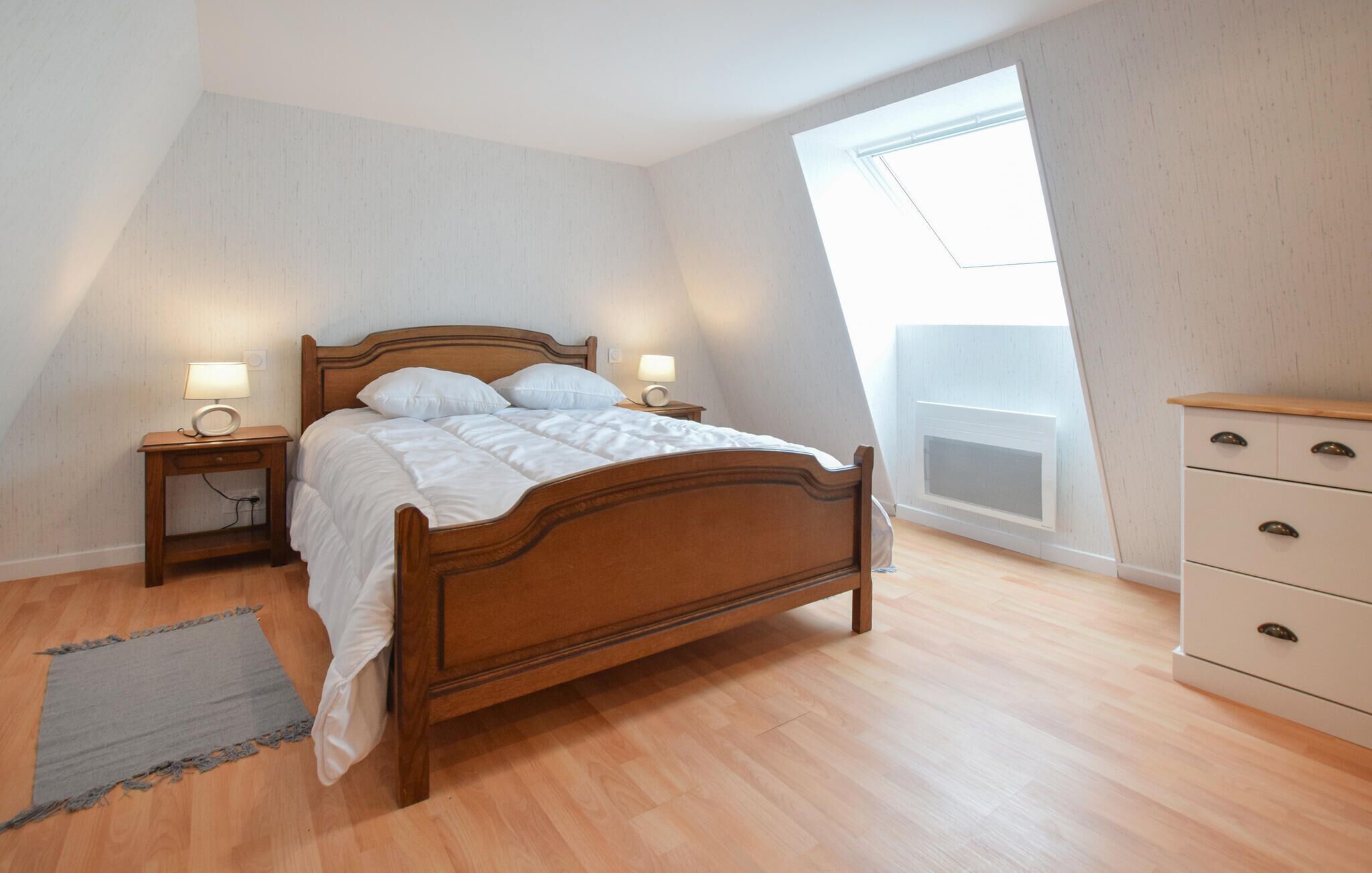 Een slaapkamer met een houten bed, bedlampen, een dressoir en een dakraam.