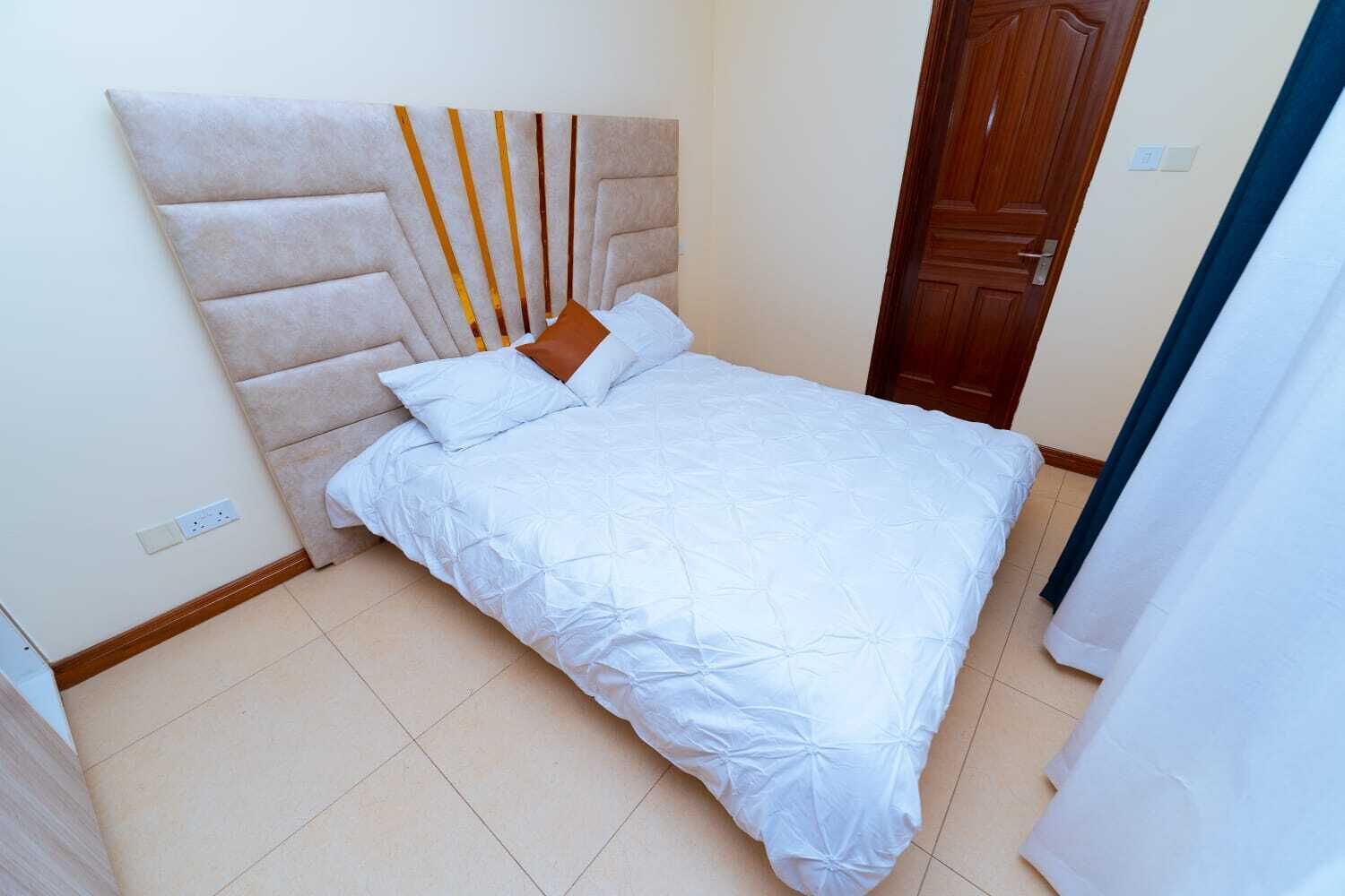 Una camera da letto con un letto, una testiera, una porta in legno e un pavimento piastrellato.
