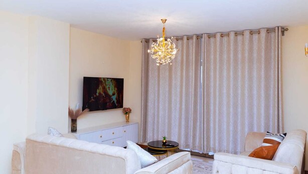 Un salon avec deux canapés blancs, un lustre, un tableau au mur et une grande fenêtre avec des rideaux.