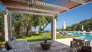 A covered outdoor seating area with a view of a swimming pool and greenery.