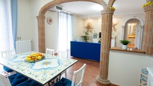 Zona pranzo con tavolo apparecchiato per quattro persone, un divano blu e una cucina visibile tramite un arco.