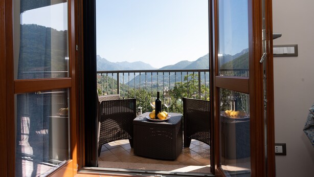 Un balcone con mobili in vimini, una bottiglia e dei bicchieri, con vista su un paesaggio montuoso.