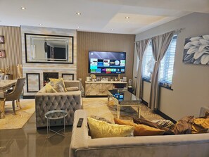 Relax in this stylish living room with a large flat-screen TV, tufted sofa, and dining area.