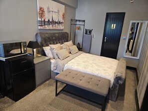 Relax in a spacious room with a large bed, bedside table, and mini-fridge.