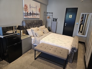 Relax in a spacious room with a large bed, bedside table, and mini-fridge.