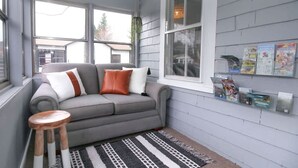 Ein gemütliches Wohnzimmer mit einem grauen Sofa, einem gemusterten Teppich und einem hölzernen Hocker.