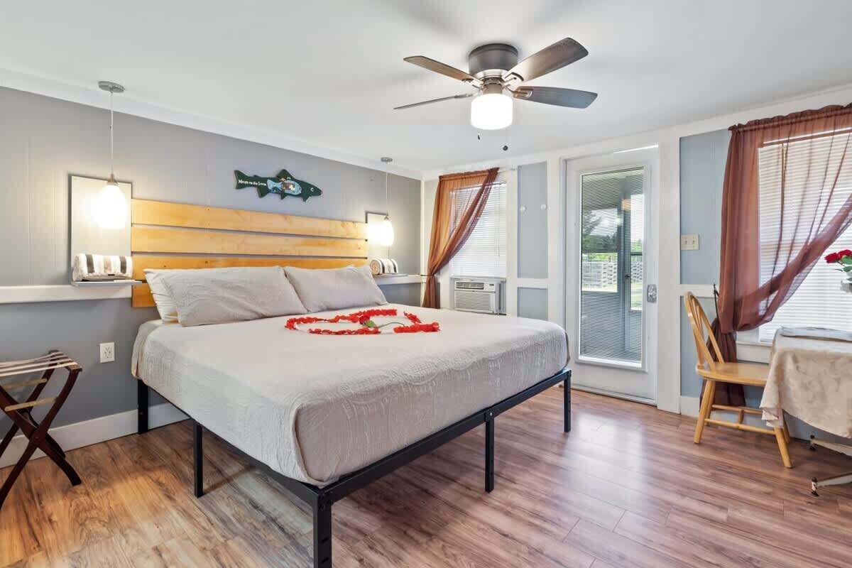 A bedroom with a bed, a ceiling fan, a window with curtains, and a table with a chair.