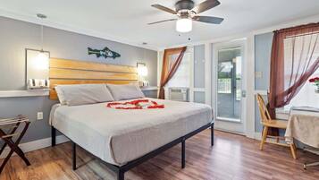 A bedroom with a bed, a ceiling fan, a window with curtains, and a table with a chair.
