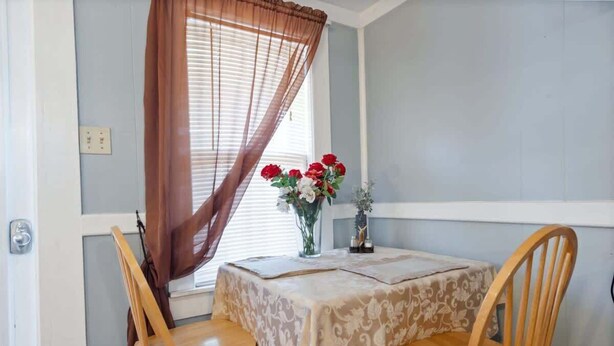A dining area with a table set for two, a window with blinds, and a vase with flowers. - Mountain views Hiking by Day & Hot tub by night #2 (Carroll)