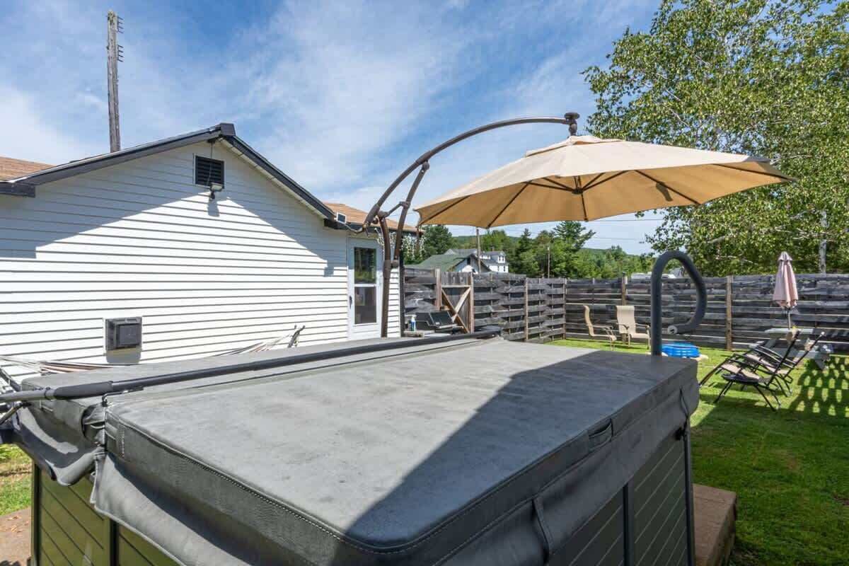 Een overdekt terras met een grote parasol, buitenmeubels en een huis op de achtergrond.