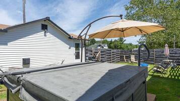 Een overdekt terras met een grote parasol, buitenmeubels en een huis op de achtergrond.