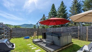 A backyard with a hot tub, a barbecue grill, and a wooden fence.