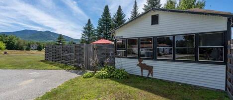 A single-story building with large windows, a fenced yard, and a mountain in the background.