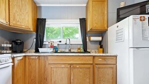 A kitchen with wooden cabinets, a white refrigerator, a stove, and a window with curtains.