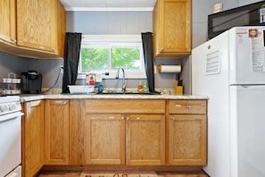 Une cuisine avec des meubles de rangement en bois, un réfrigérateur blanc, une cuisinière et une fenêtre avec des rideaux.
