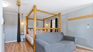A room with a four-poster bed, a grey sofa, wooden flooring, and a wall-mounted light fixture.