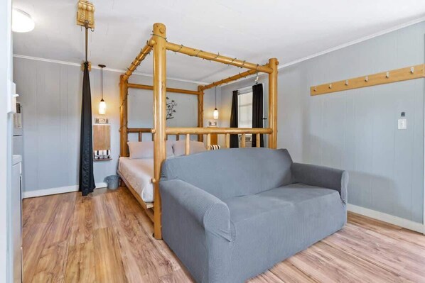 A room with a four-poster bed, a grey sofa, wooden flooring, and a wall-mounted light fixture.