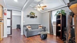 Una sala de estar con un sofá gris, una mesa de centro de vidrio, un ventilador de techo y una chimenea.