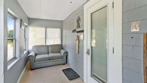 Una habitación con un sofá gris, una puerta con un panel de vidrio y una ventana con persianas.